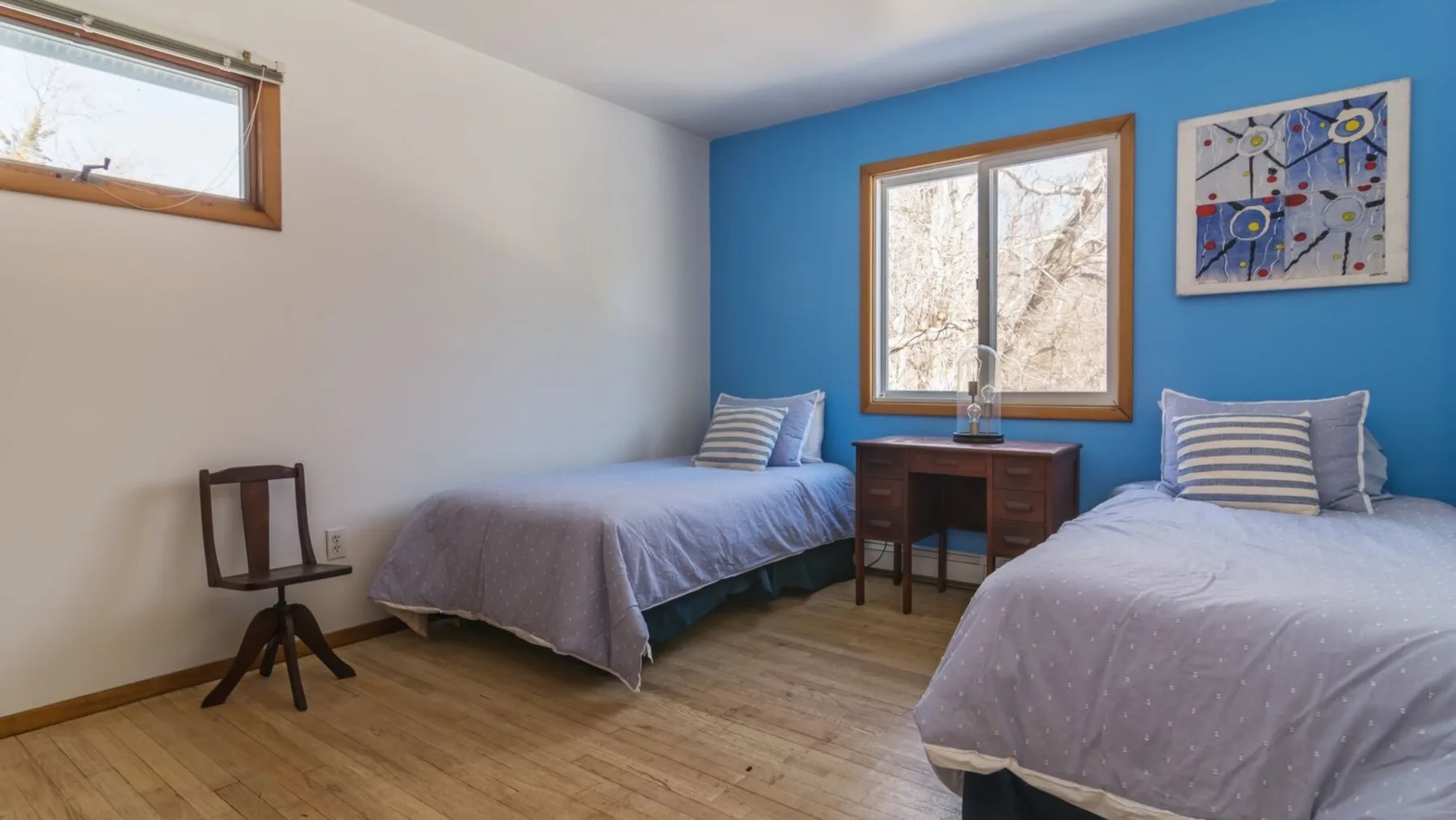 A bedroom with two beds, a blue accent wall, and framed artwork.