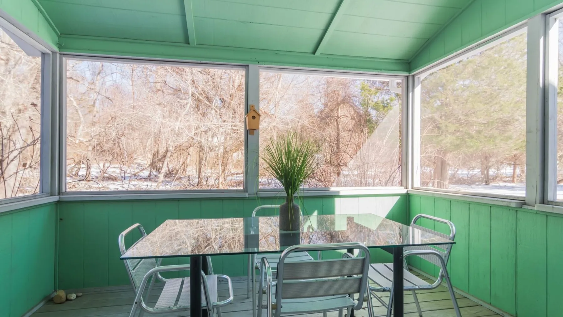 A bright enclosed porch with green walls, glass windows, and a dining table.