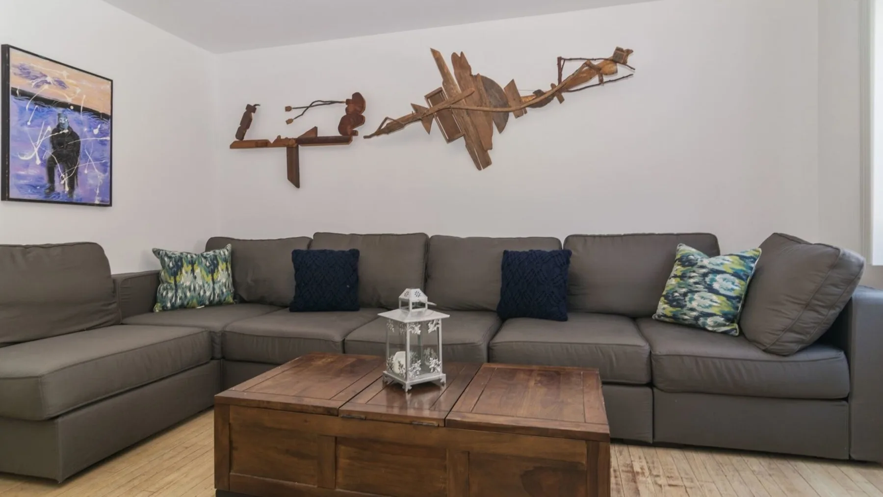 A living room with a sectional sofa, wooden coffee table, and wall art.
