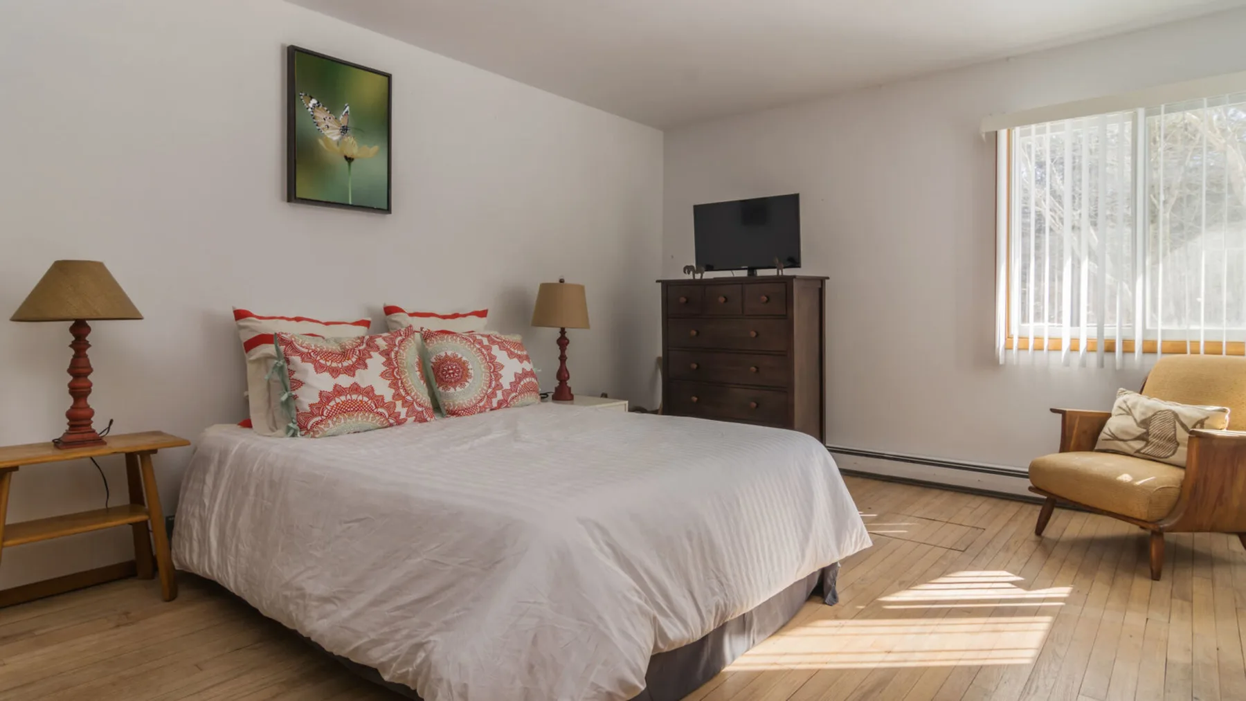 A bedroom with a large bed, dresser, and a chair beside the window.