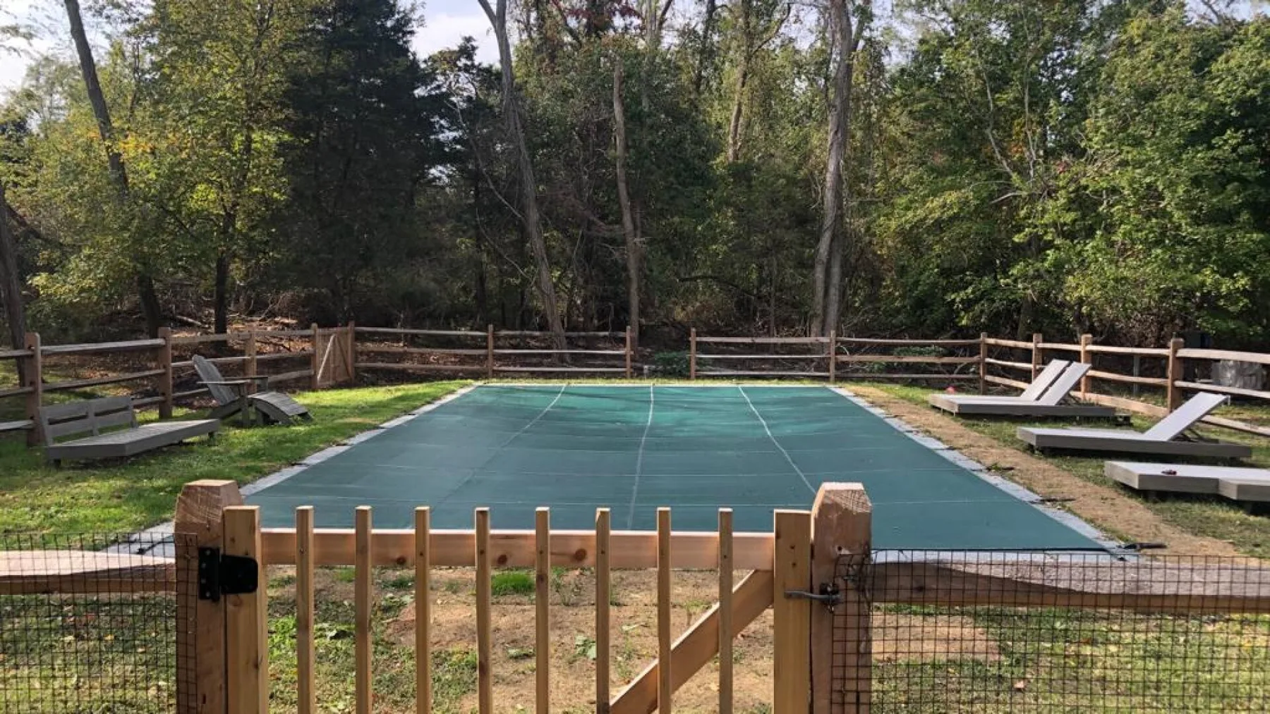 An outdoor court with a green surface, bordered by trees and wooden fencing.