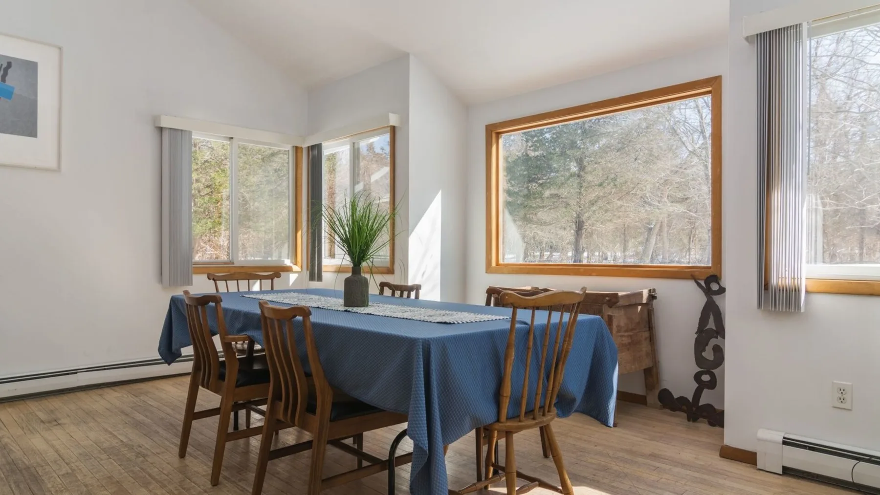A dining room with a long table covered in a blue cloth beside large windows.