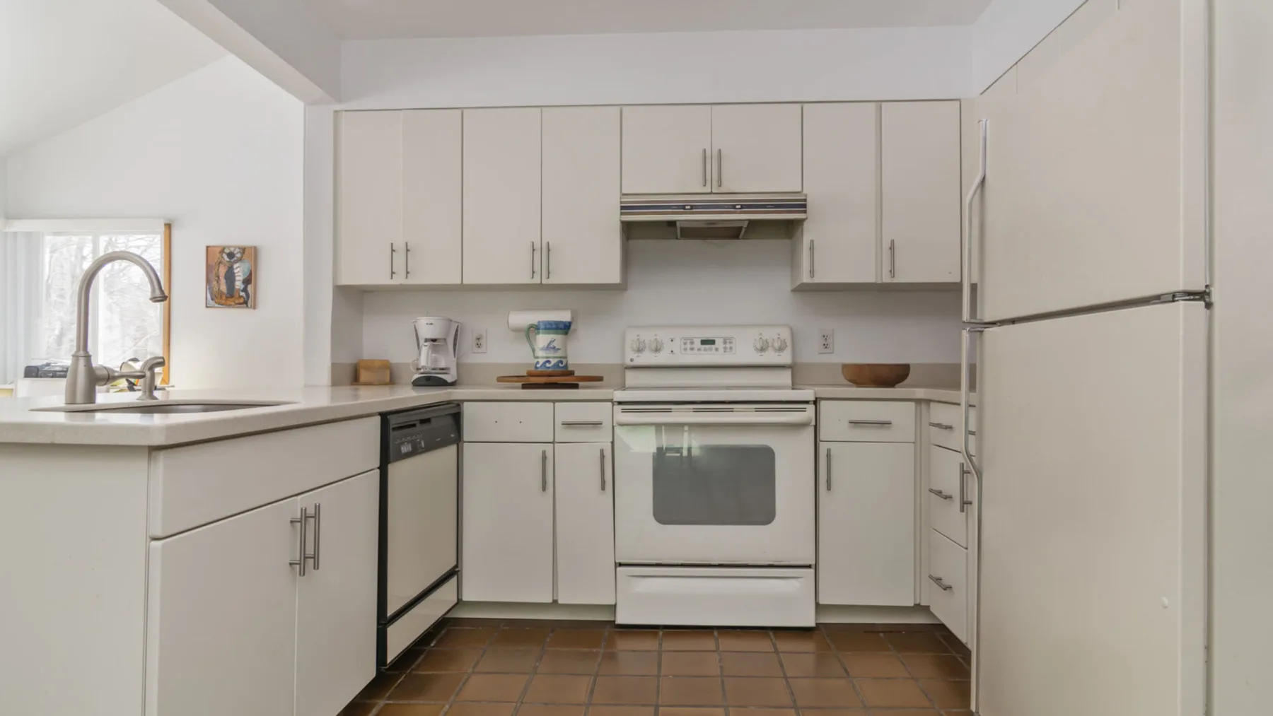 A bright kitchen with white cabinetry, an oven, and a large refrigerator.