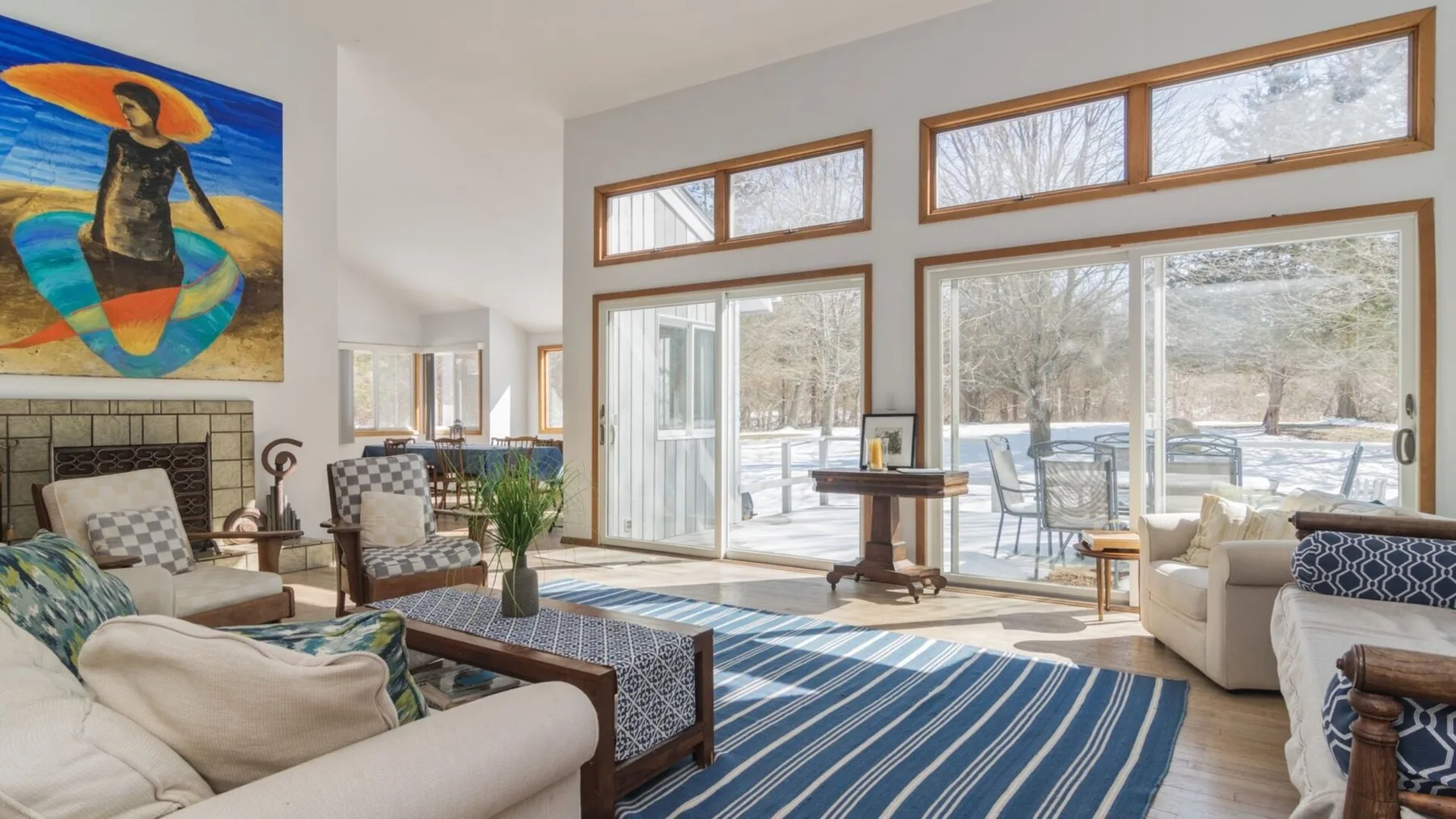 A bright living room with large windows, seating, and a striped rug.