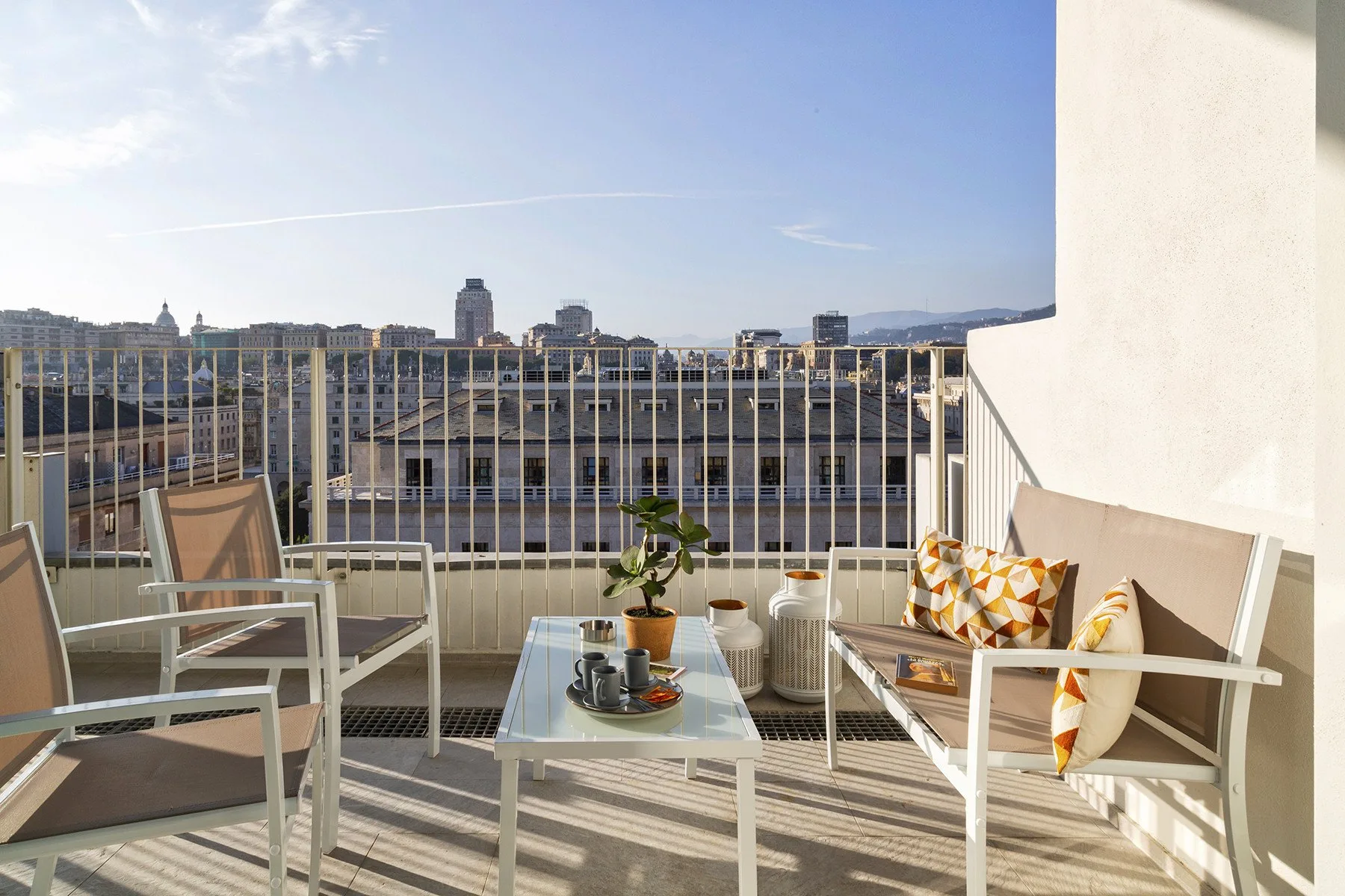 Una zona de estar en un balcón soleado mira hacia edificios de la ciudad.