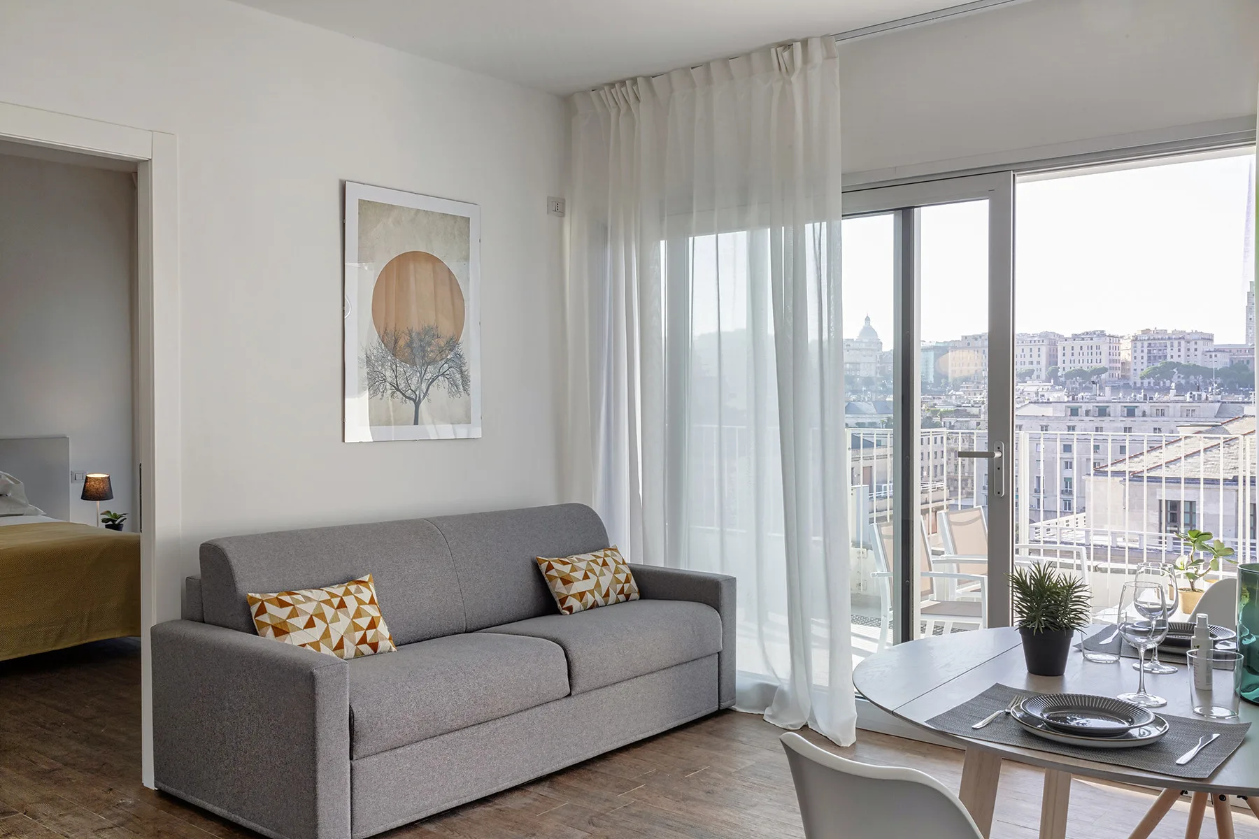 A living room with gray seating beside large windows overlooking nearby buildings.