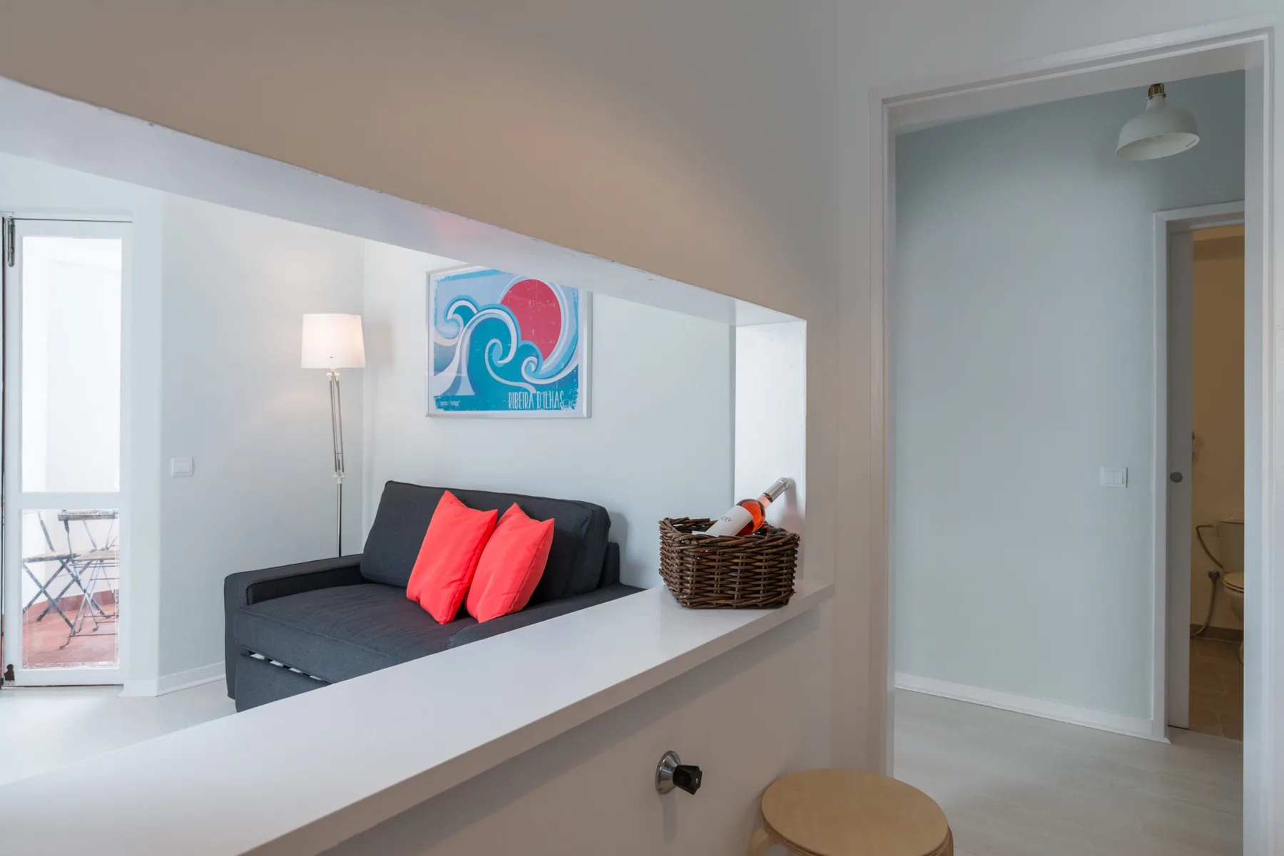 A living area with dark seating, colorful cushions, and a framed wave print.