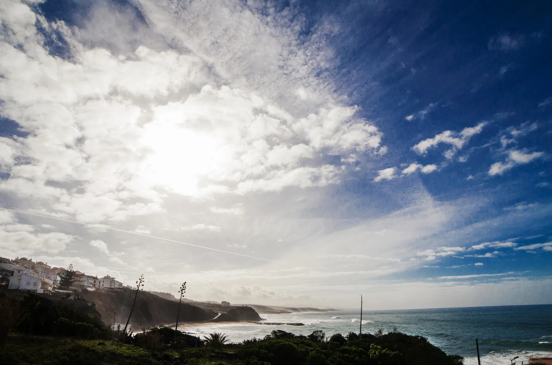 Coastal landscape with ocean waves, a distant shoreline, and a cloudy sky.
