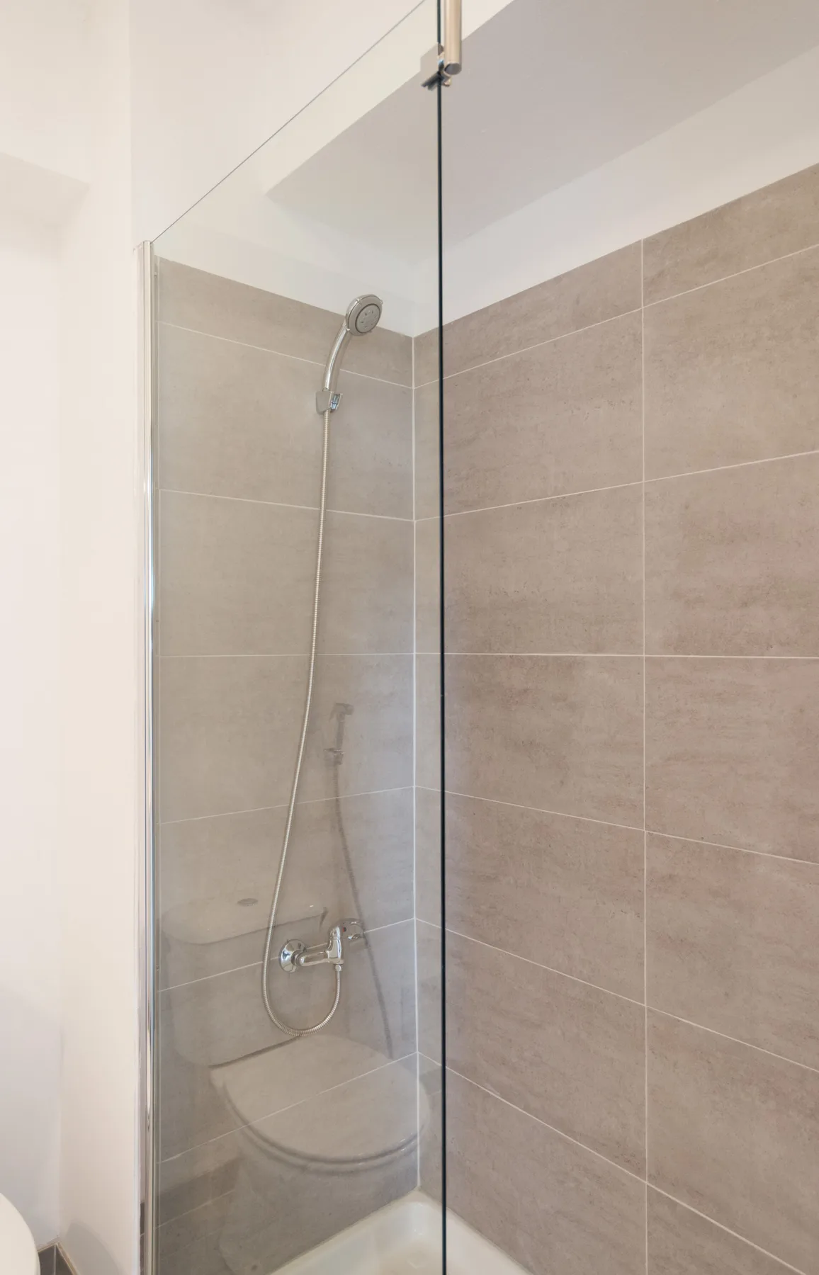 A tiled shower with a handheld showerhead and glass screen.