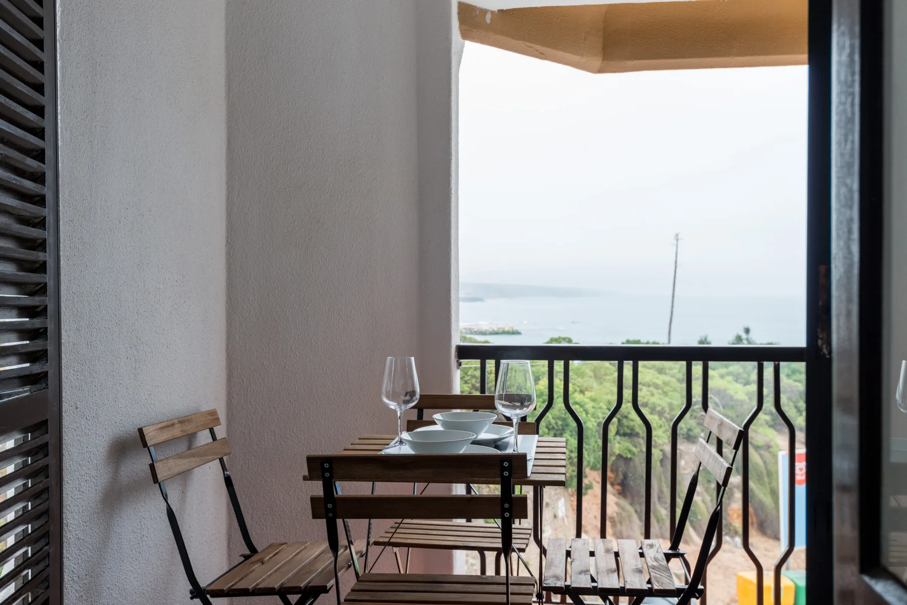 A balcony dining area with a small table and chairs overlooking the coast.