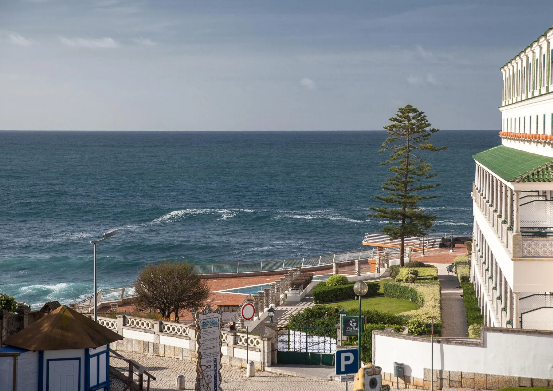 A coastal view overlooks the ocean, a seaside promenade, and nearby buildings.