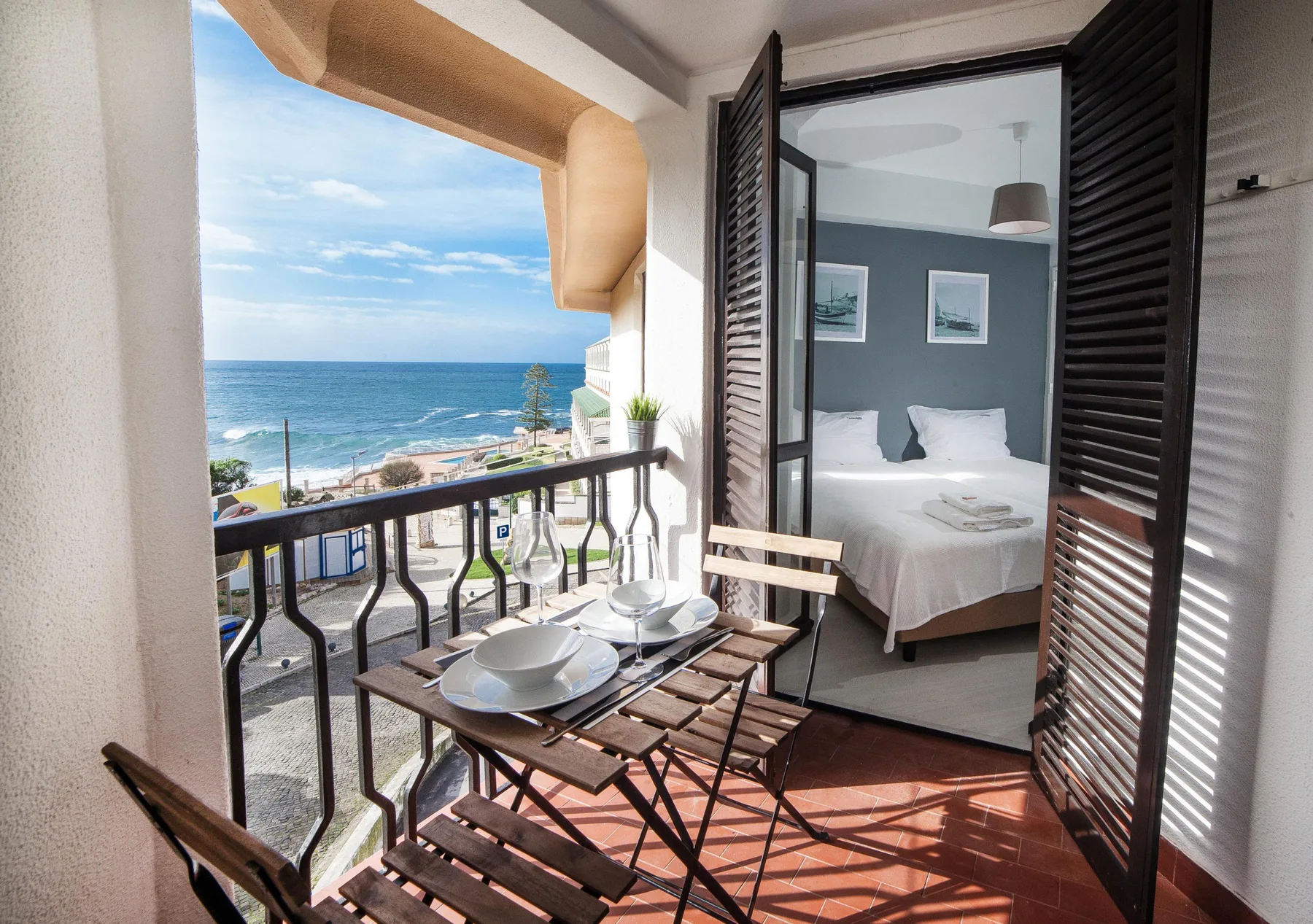 A balcony dining area overlooks the ocean, with a bedroom visible through open shutters.