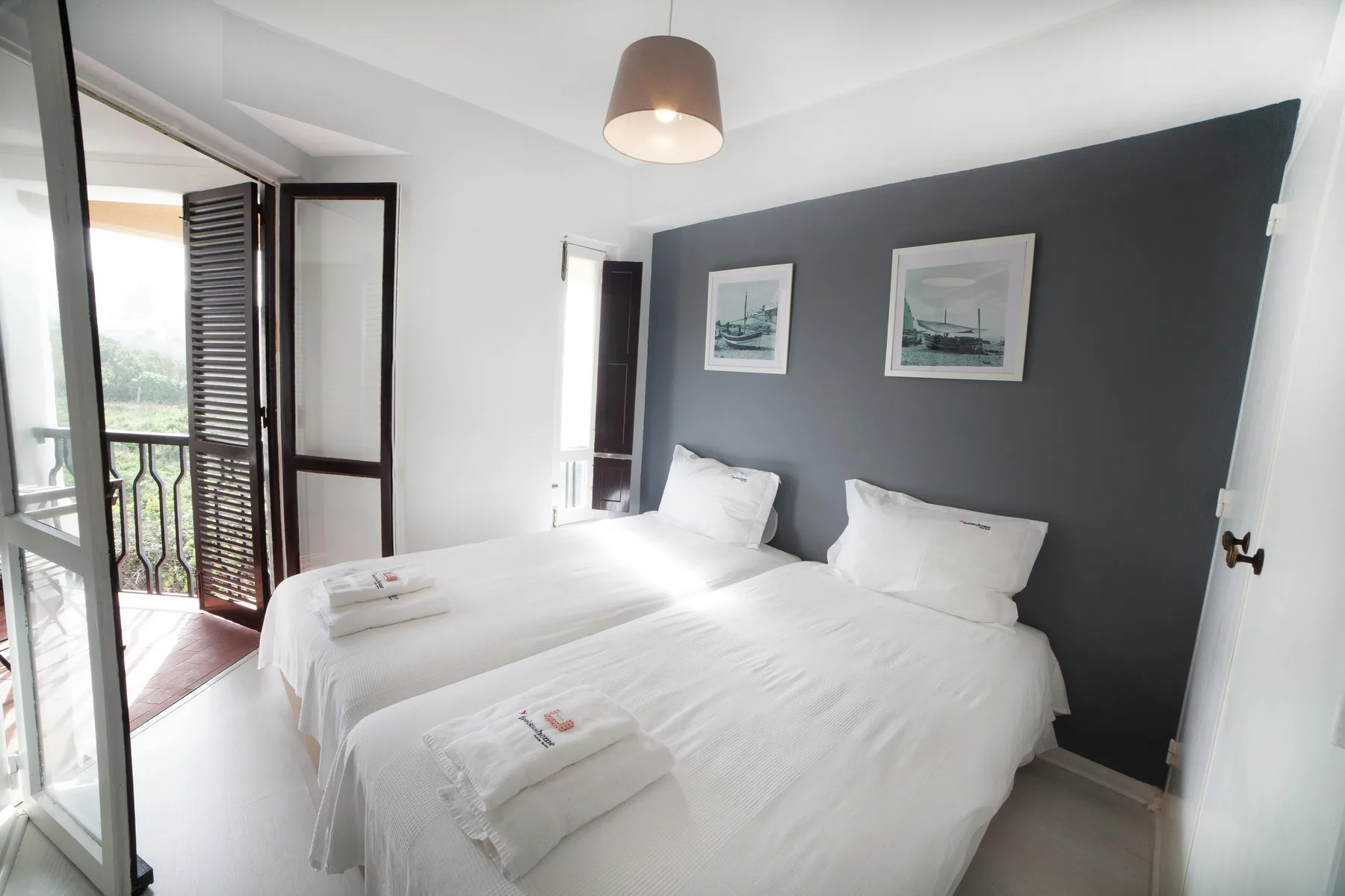 A bedroom with two beds, white linens, and framed pictures on a dark accent wall.