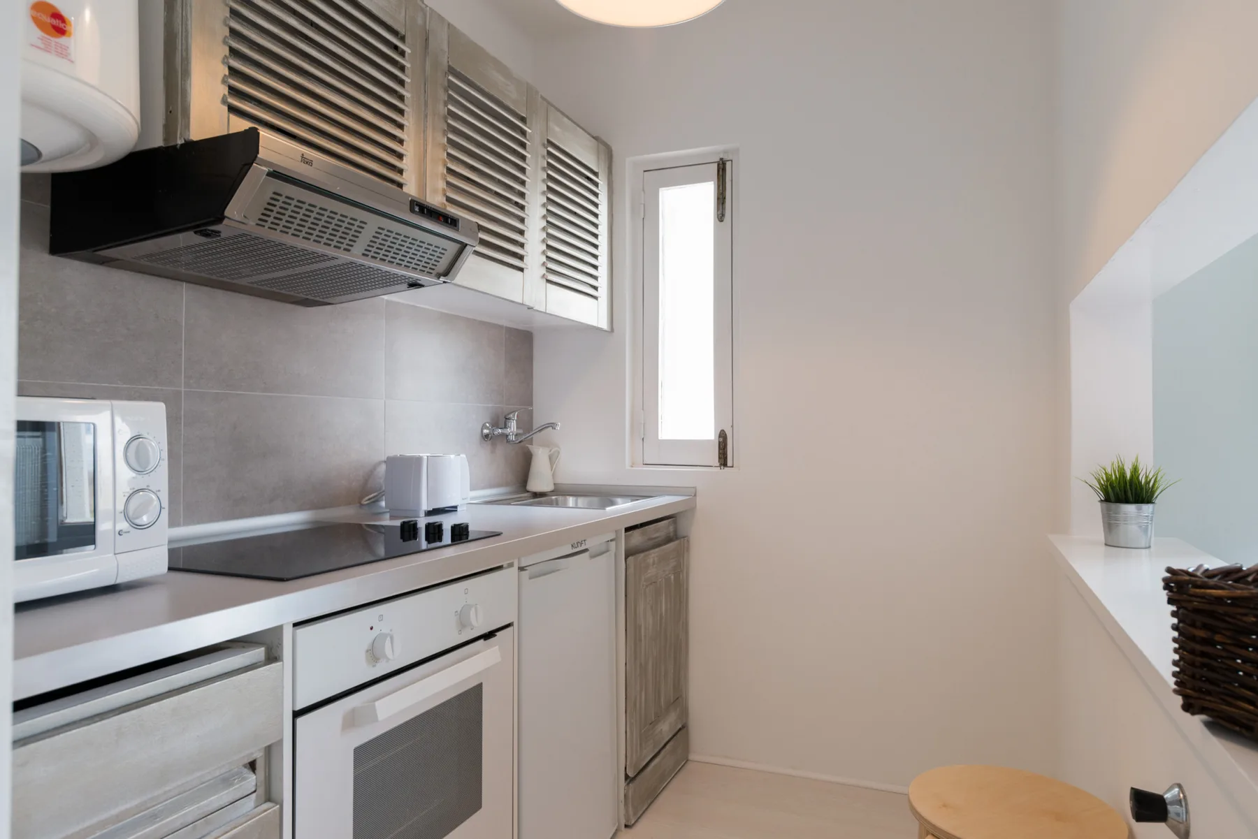 A compact kitchen with light cabinetry, countertop appliances, and a narrow window.