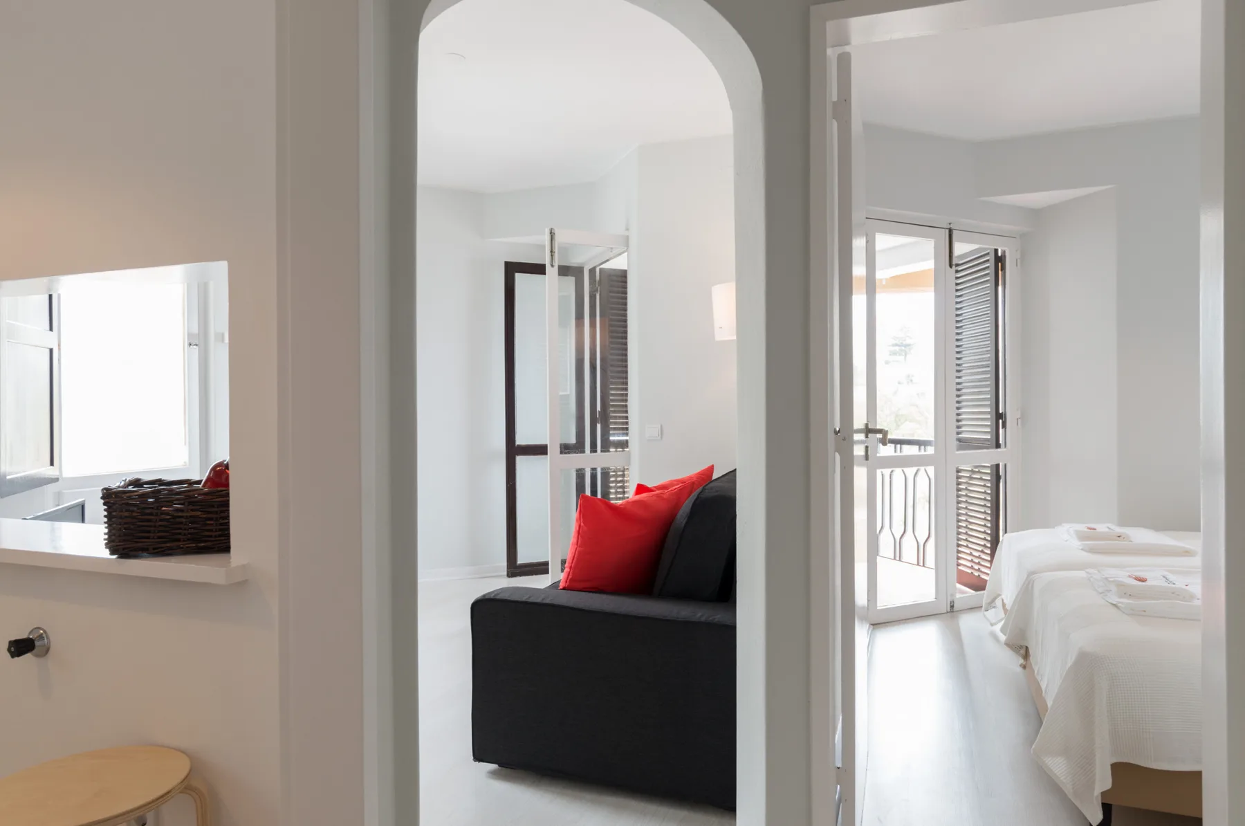 An apartment interior with a dark seating area and a bedroom visible through an open doorway.