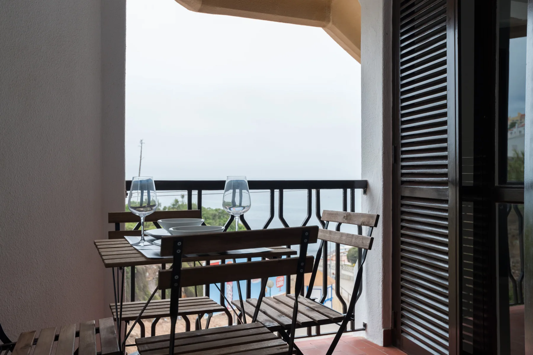 A small balcony with a table and seating overlooks the sea.