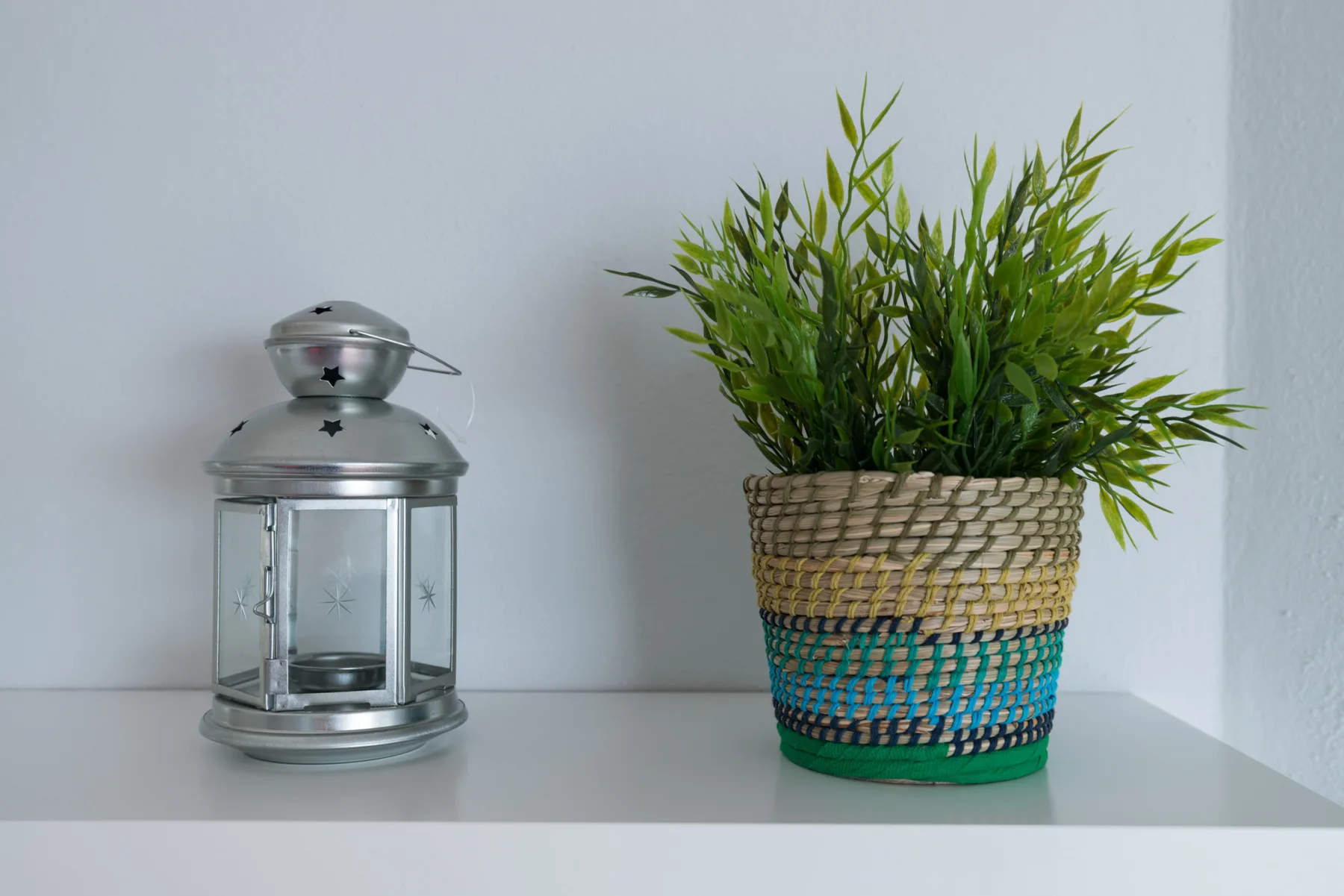 A potted green plant and a metal lantern sit on a white shelf.