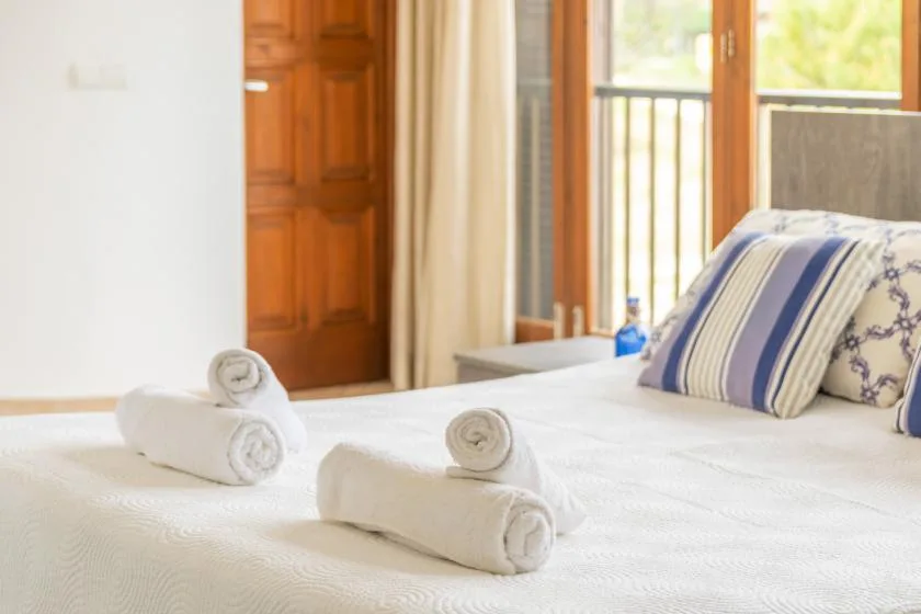 A bedroom with a neatly made bed, folded towels, and a balcony door.