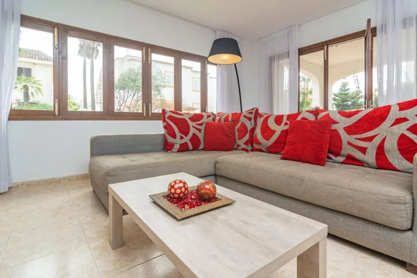 A bright living room with a gray sectional sofa and red patterned cushions.
