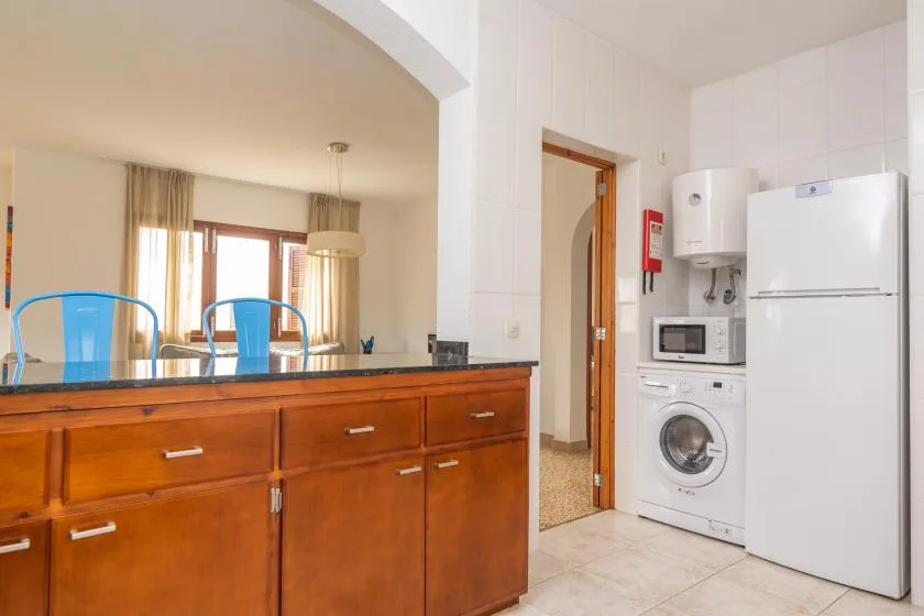 A kitchen with wooden cabinets, a refrigerator, and laundry appliances.