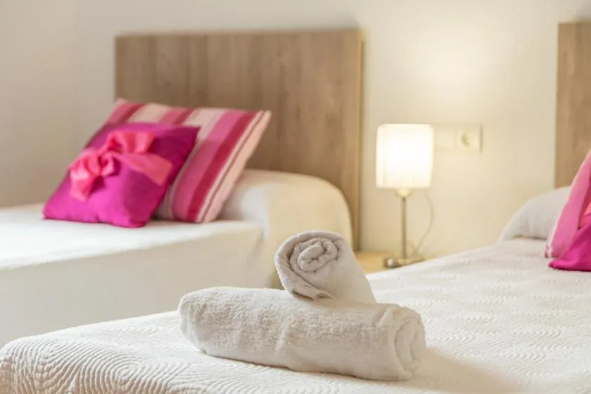 A bedroom with two beds, pink pillows, and neatly folded towels.