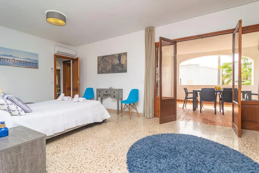 A bedroom with a bed, blue seating, and open wooden doors to a dining area.
