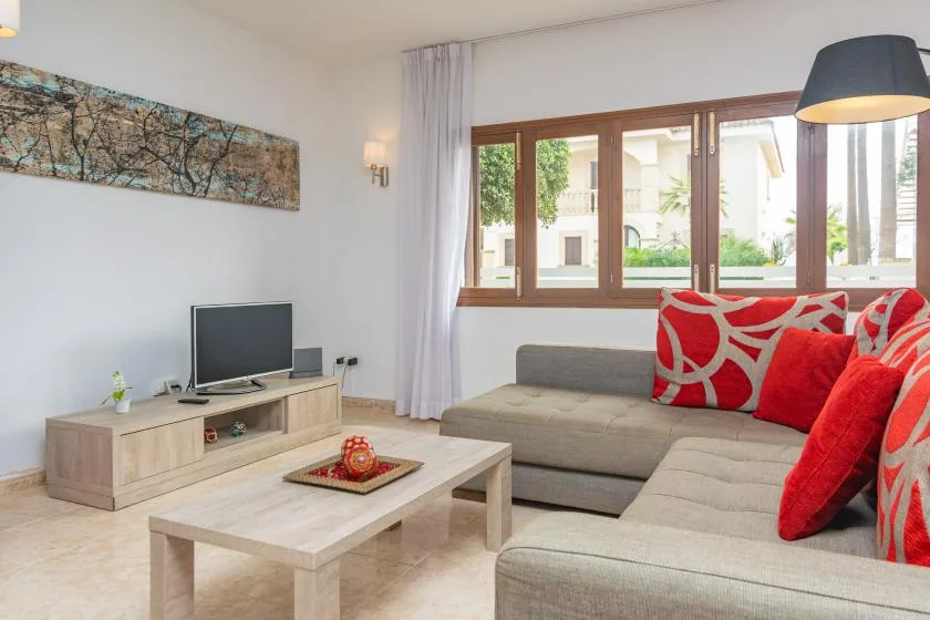 A living room with a sectional sofa, coffee table, and windows overlooking greenery.