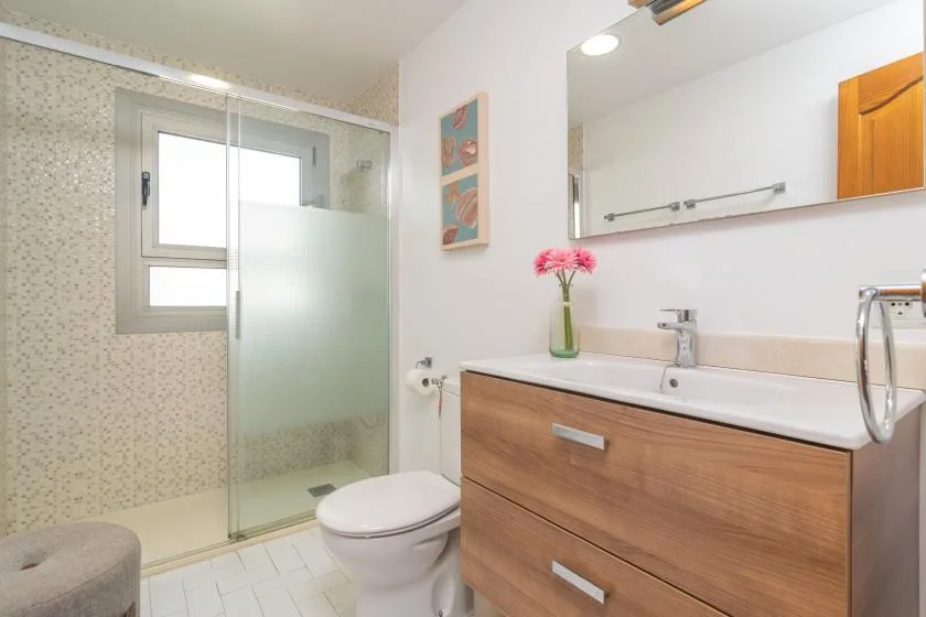 A bright bathroom with a glass shower, toilet, and wood-front vanity.
