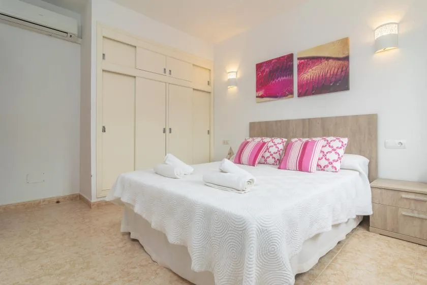 A bright bedroom with a neatly made bed and pink decorative pillows.