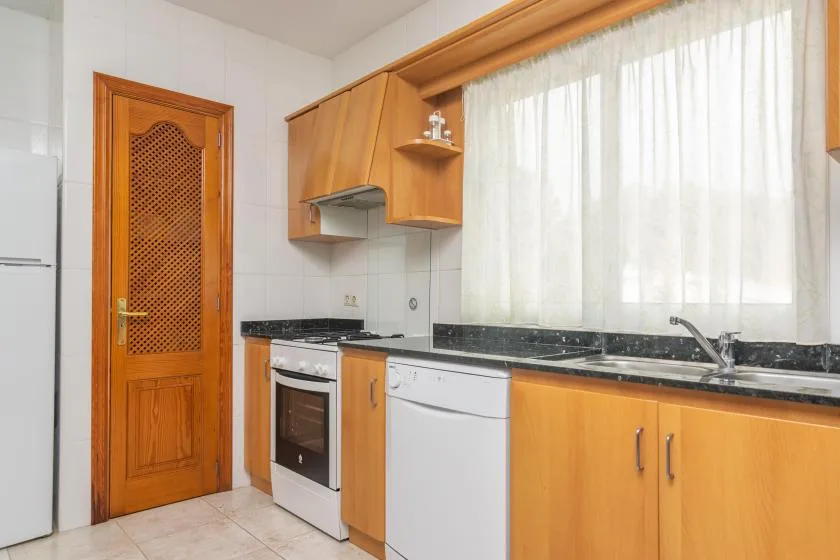 A bright kitchen with wooden cabinets, a stove, and a large curtained window.