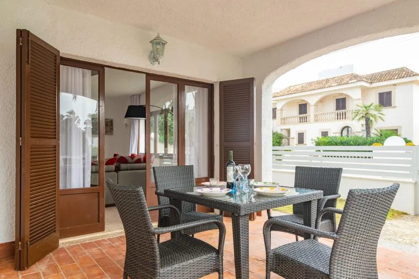 A covered patio has a dining table and seating beside open doors.