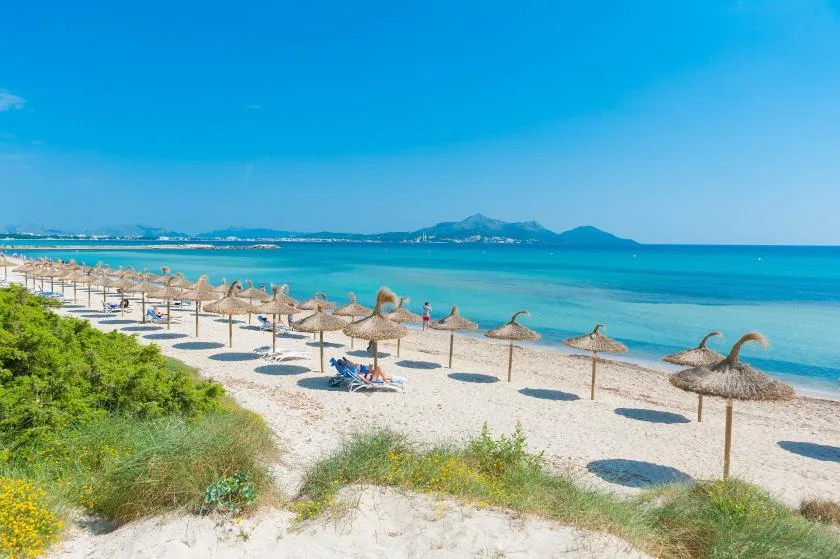 A sandy beach lined with thatched parasols overlooks clear turquoise water.