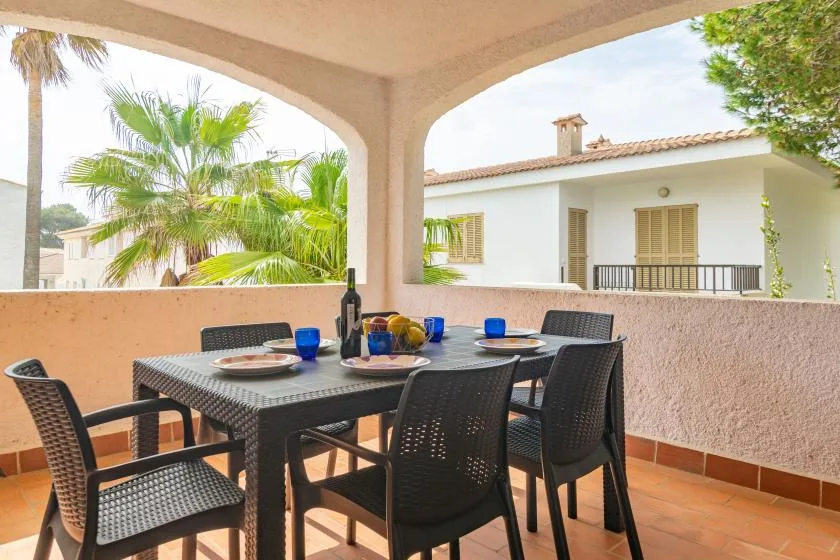 A covered outdoor dining area with a table and seating overlooks palm trees and a neighboring house.