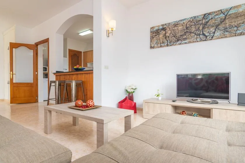 A bright living room with a television, low table, and seating beside an open kitchen.