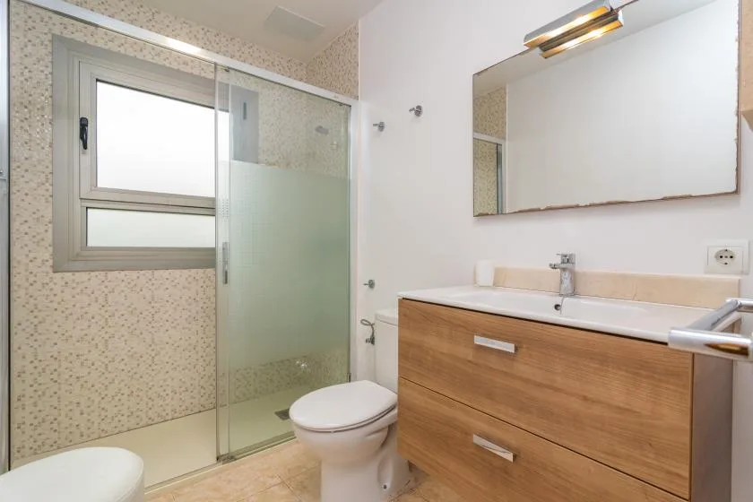 A bathroom with a glass shower, toilet, and wooden vanity.