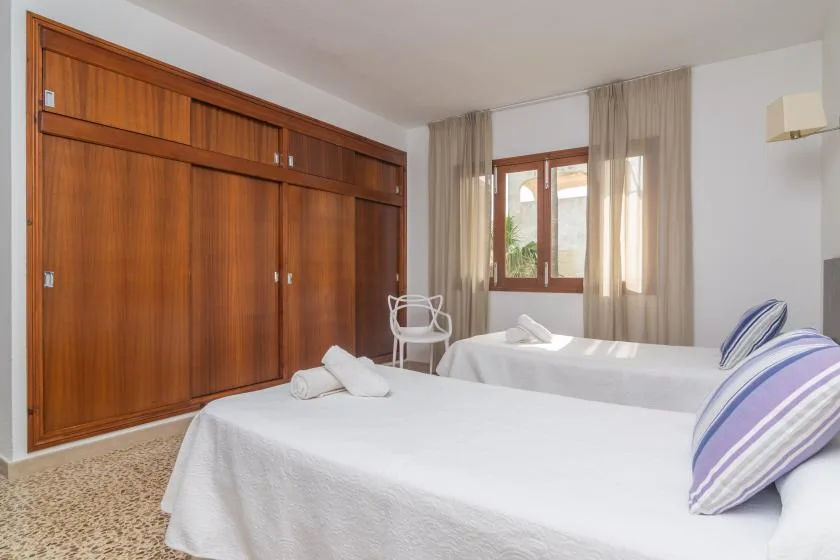 A bedroom with two beds, wooden wardrobes, and a curtained window.