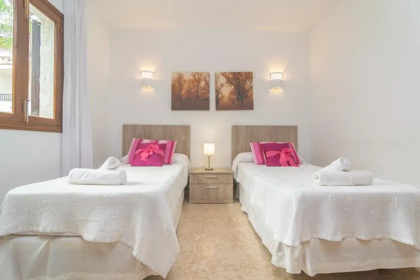 A bright bedroom with two single beds and matching pink accent pillows.