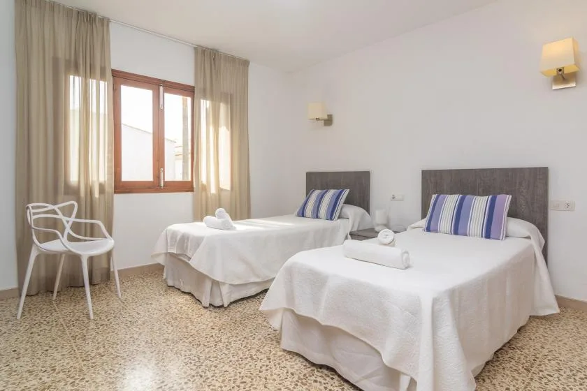 A bright bedroom with two beds and a large window with curtains.