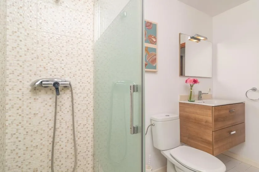A bathroom with a glass shower, toilet, and wood-toned vanity.