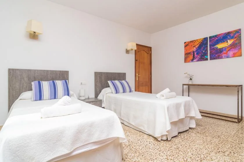 A bright bedroom with two beds, white bedding, and colorful wall art.