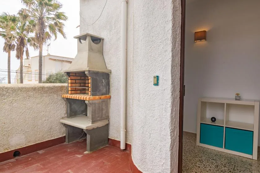 A tiled outdoor patio with a built-in barbecue beside an open doorway.