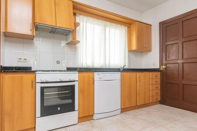 A bright kitchen with wooden cabinets, a stove, and a dishwasher beneath the window.