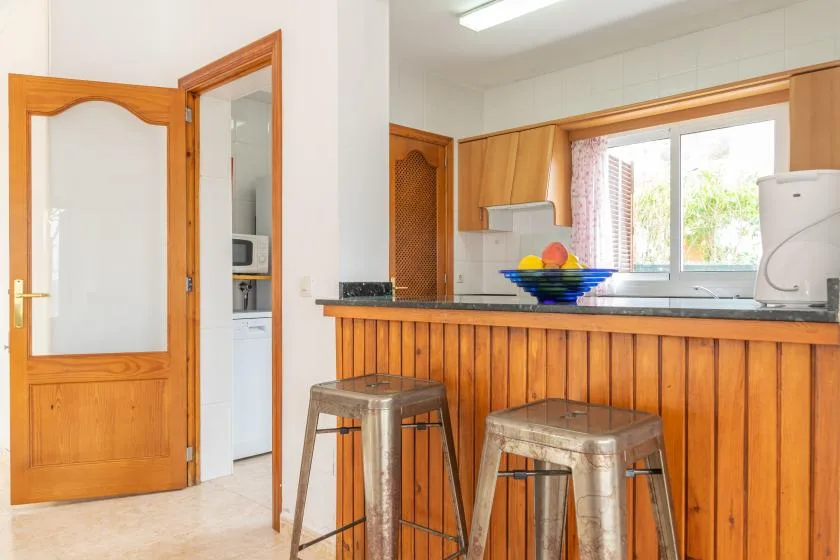 A kitchen counter with wooden paneling, metal stools, and a window above the sink.