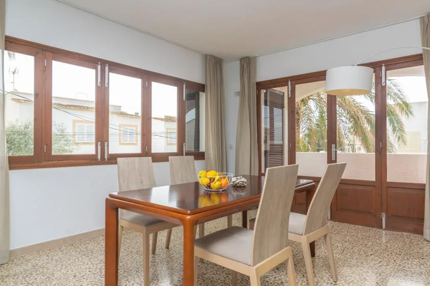 A dining area with a wooden table and chairs beside large windows.