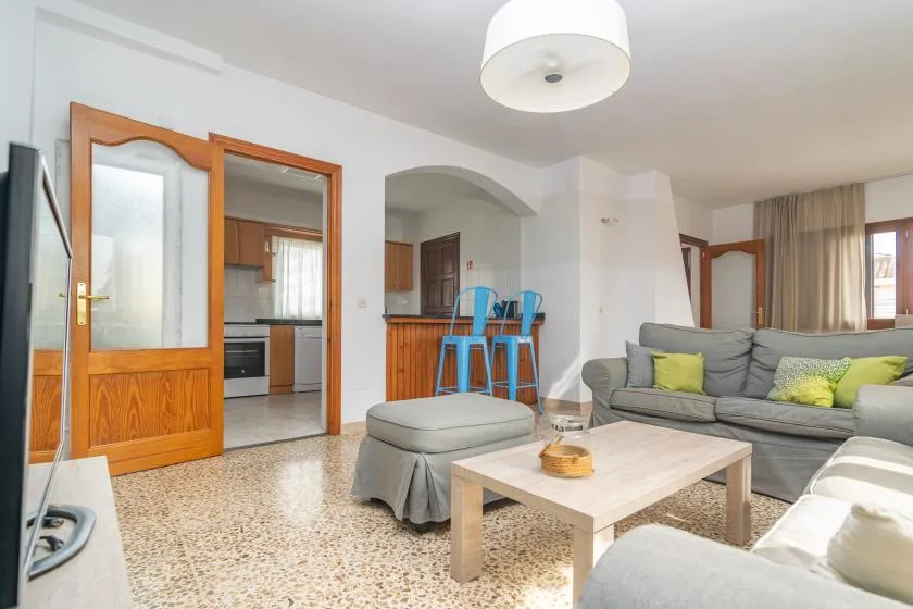 A living room with gray seating, a coffee table, and a kitchen visible through an archway.