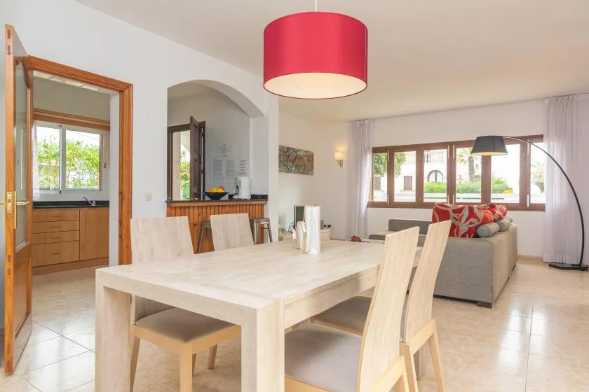 A bright open-plan dining and living area with a pale dining table and large windows.