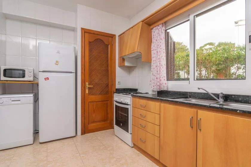 A bright kitchen with wooden cabinets, appliances, and a window overlooking greenery.