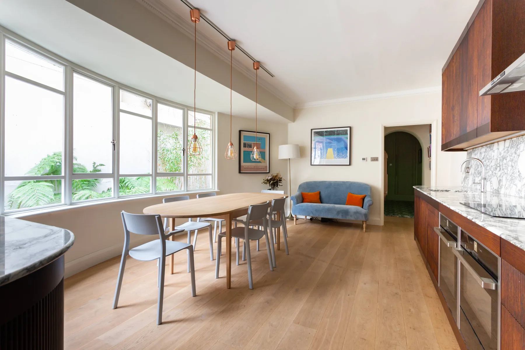 A bright dining area beside a kitchen, with a long table and blue seating.