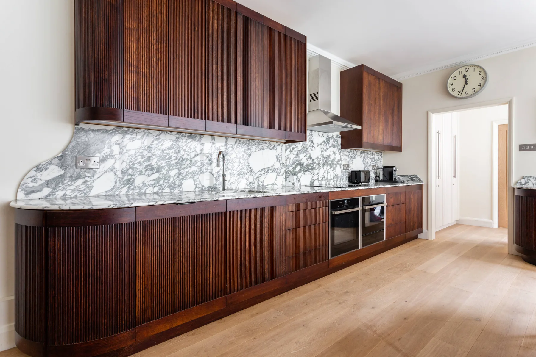 A kitchen with dark wood cabinets, a marble-patterned backsplash, and built-in appliances.