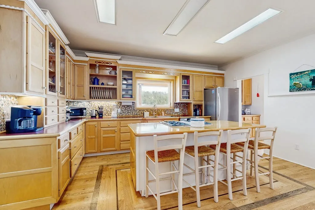 Una cocina luminosa con gabinetes de madera clara y una isla central con asientos.